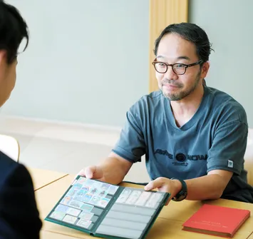 買取訪問のために自宅へ来たバイセルの社員に切手のコレクション手帳を手渡している男性の写真